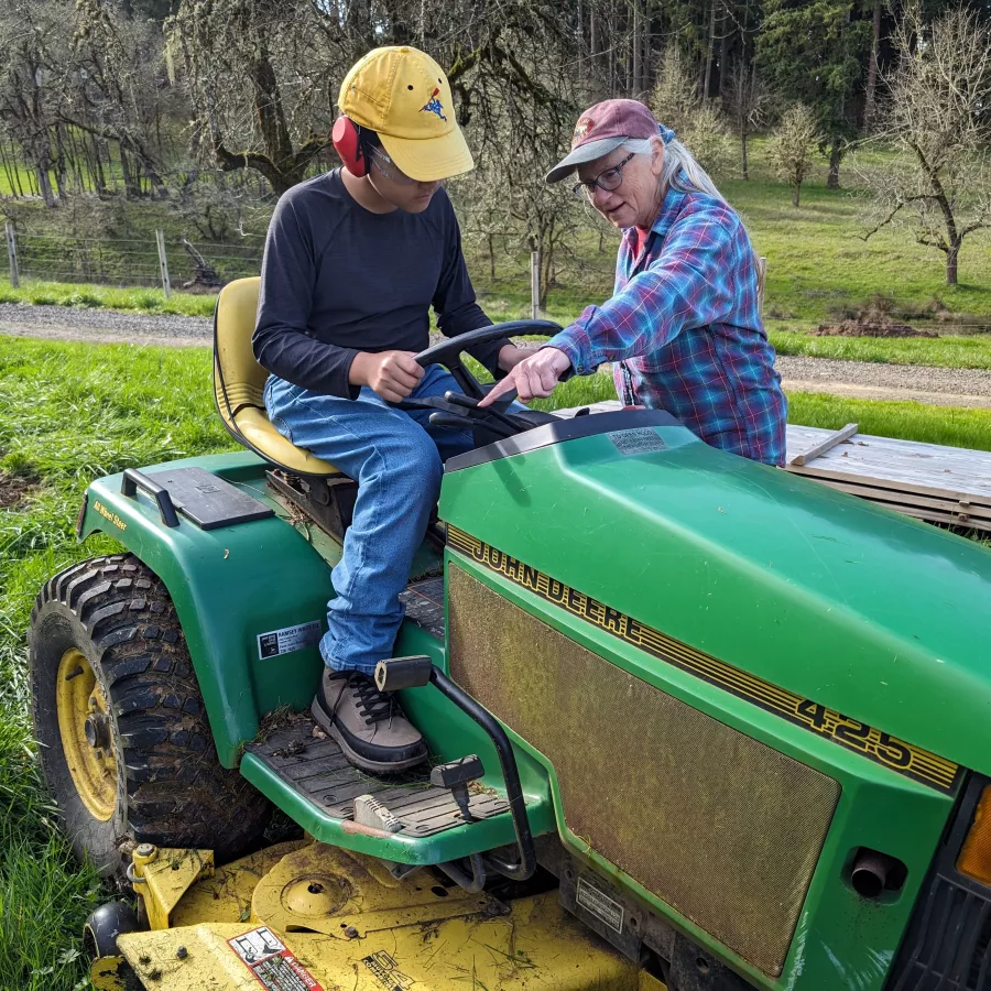 adults teaches child to use a riding mower
